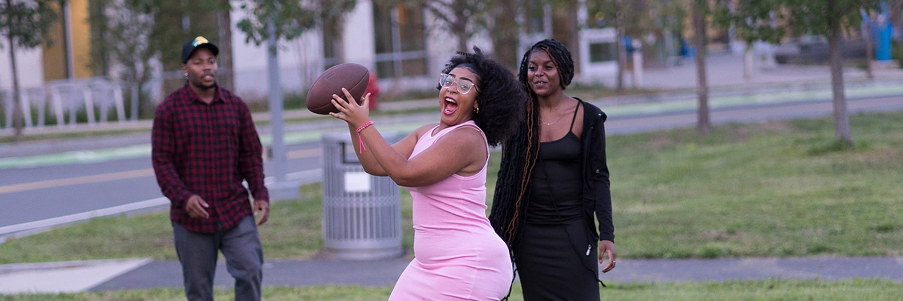 Girl in pink dress catches football at First Friday event Campus Center lawn.