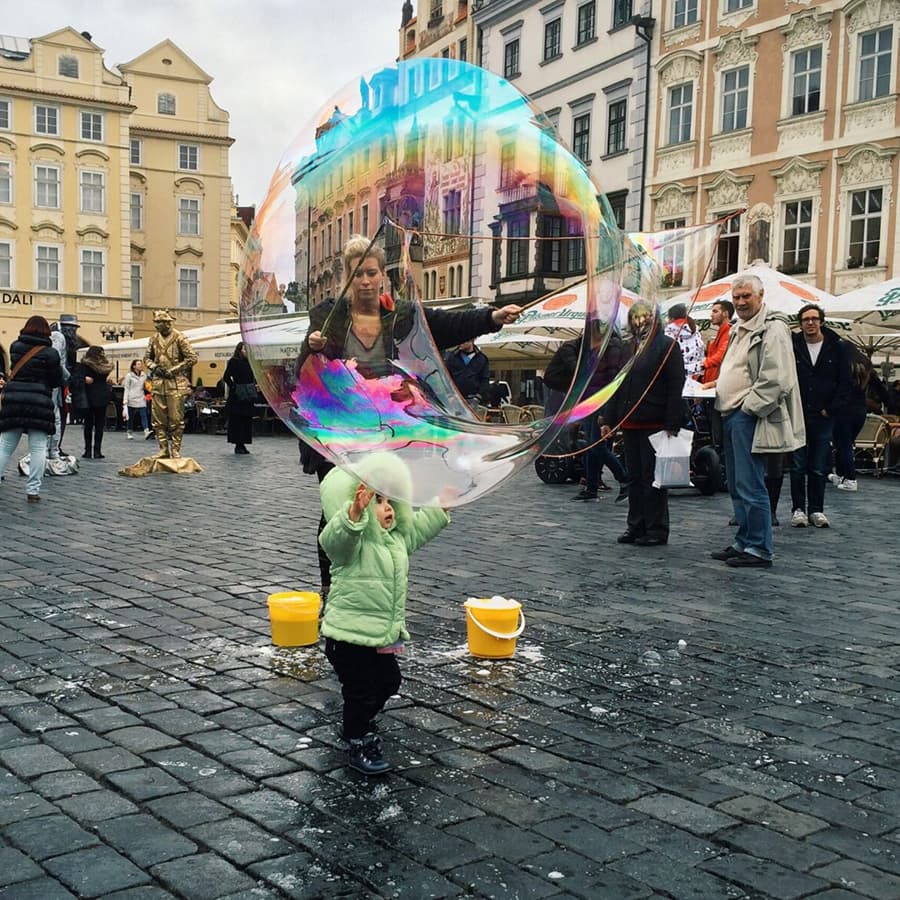 child blows giant rainbow bubble on plaza in Europ