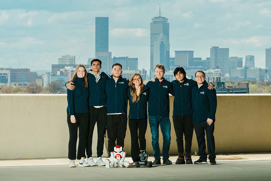 seven students and two robots are standing on a rooftop infront of the city skyline