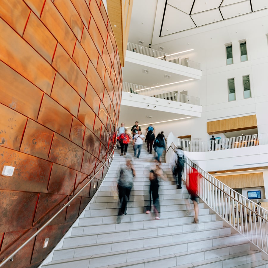 university hall interior showing students walking in blurred motion up and down the main entrance stairs