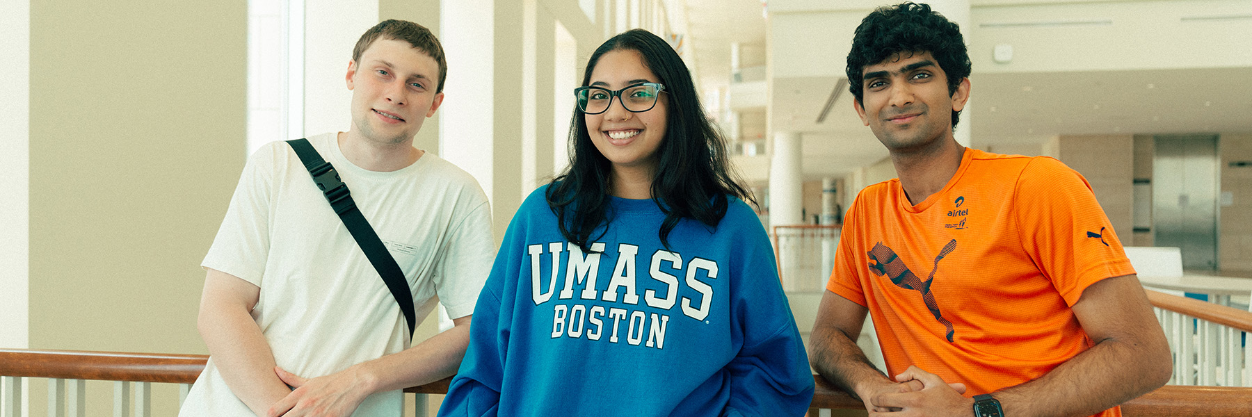 Three UMass Boston students, a woman and two men, smile in the Campus Center