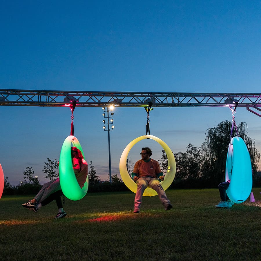 Students in neon circle swings on campus center lawn.