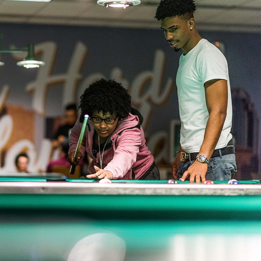 2 students play pool in the game room.