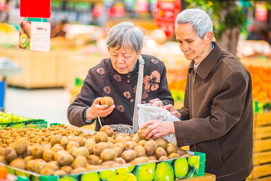Two older adults shopping for vegetables.