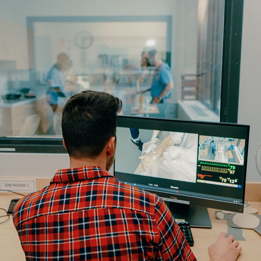 Student monitors peers working in the simulation lab on his computer in the control room.