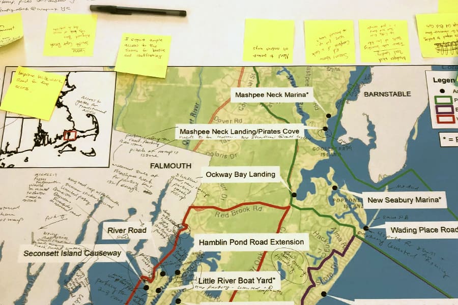 Bulletin board with a map of MA with labels on Mashpee Neck Marina, Ockway Bay Landing, River Road, Seconsett Island Causeway, New Seabury Marina, Hamblin Pond Road Extension, Little River Boat Yard, And sticky notes with writing too small too read.